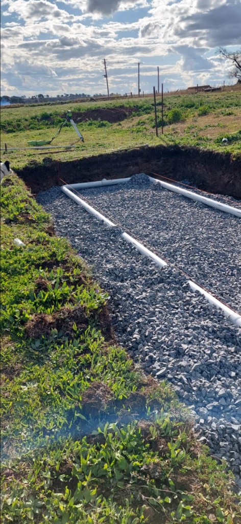 PVC drainage layout in a gravel-filled excavation on a grassy site
